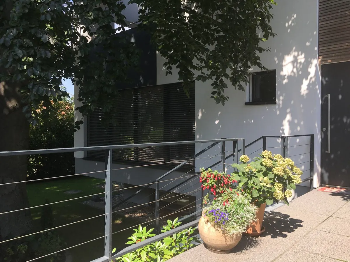 Haus D in Ingelheim: weiße Fassade, Rampe mit Geländer und Blumen